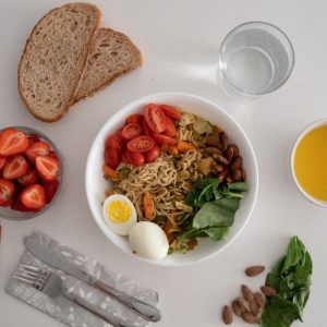 A balanced meal featuring a variety of healthy ingredients including noodles, eggs, almonds, strawberries, and fresh vegetables.